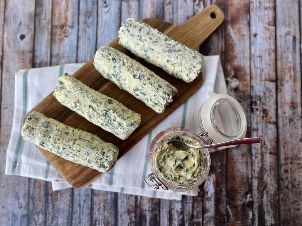 Rolls of garlic butter lined up on a wooden bar, with a small jar of garlic butter next to it.