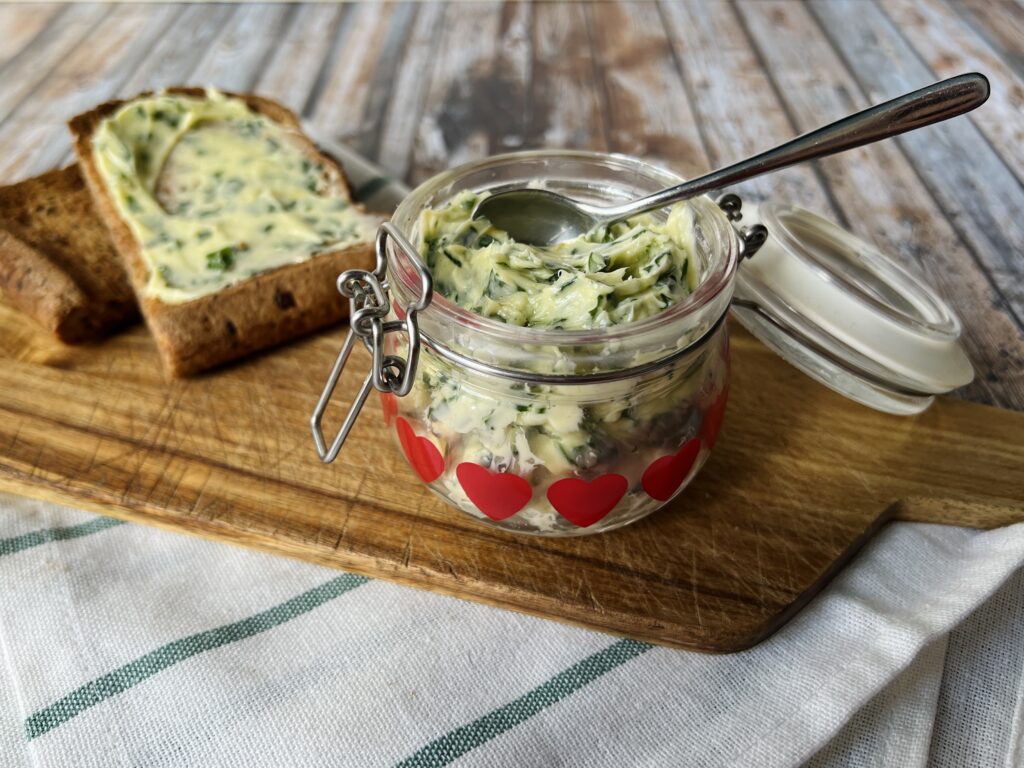 Wild Garlic Butter in a jar, sitting on a wooden board with a slice of buttered toast next to it