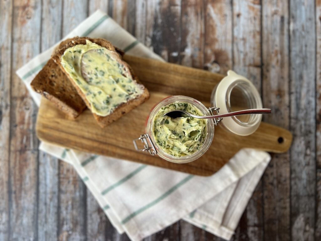 Wild Garlic Butter in a jar, sitting on a wooden board with a slice of buttered toast next to it