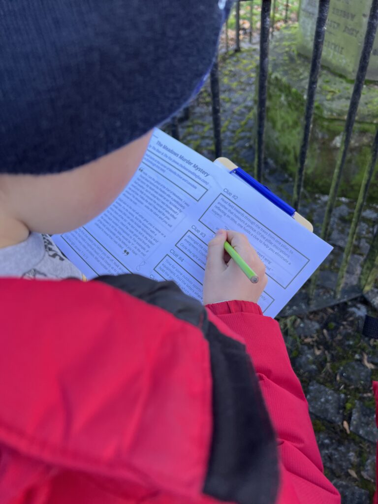 Child writing on a murder mystery trail sheet